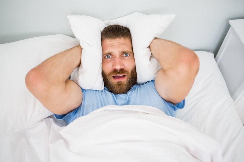 man covering ears in bed 