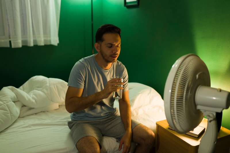 person sitting on bed next to a fan
