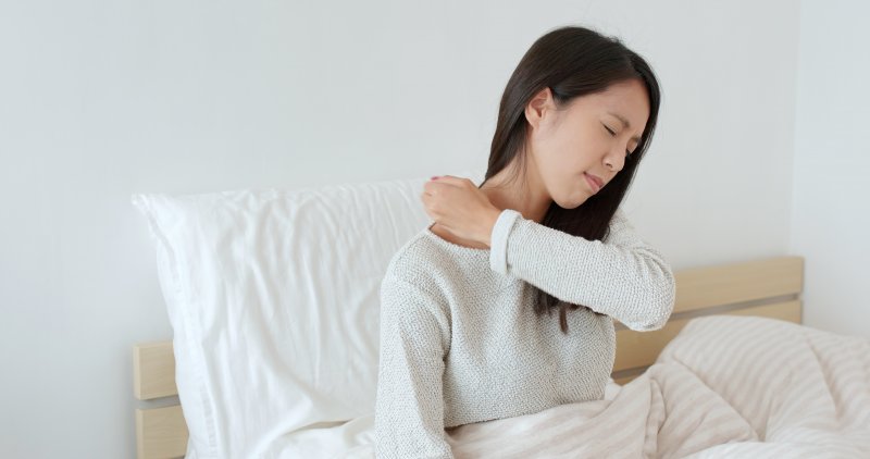 woman holding neck and shoulder in bed  