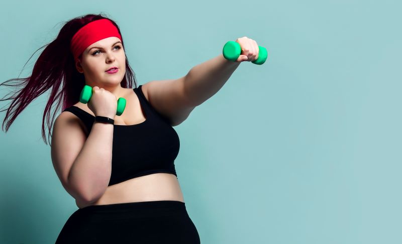 Overweight woman holding dumbbells and exercising