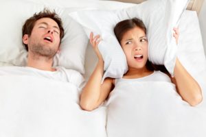man snoring and woman covering her ears irritated