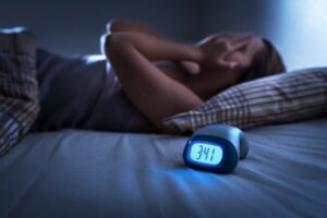 Person struggling to sleep with alarm clock in foreground.