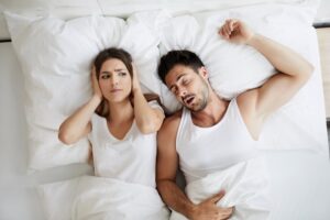 Man with sleep apnea snoring while partner covers her ears